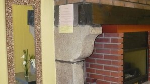Een bakstenen schoorsteen met een stenen omlijsting, een spiegel met decoratieve lijst en een tafeltje met een bloevas.