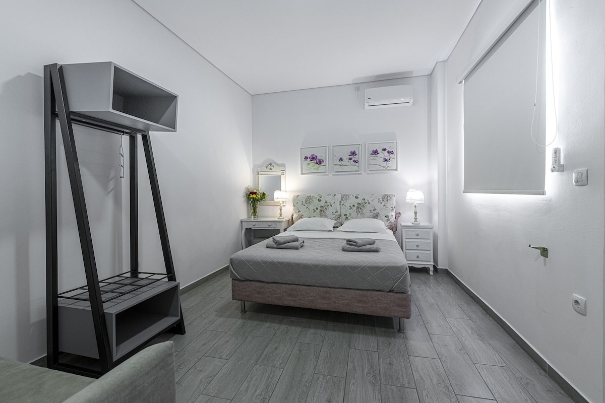 A modern bedroom with a bed, bedside tables, a nightstand, a standing lamp, and a wall-mounted shelf.