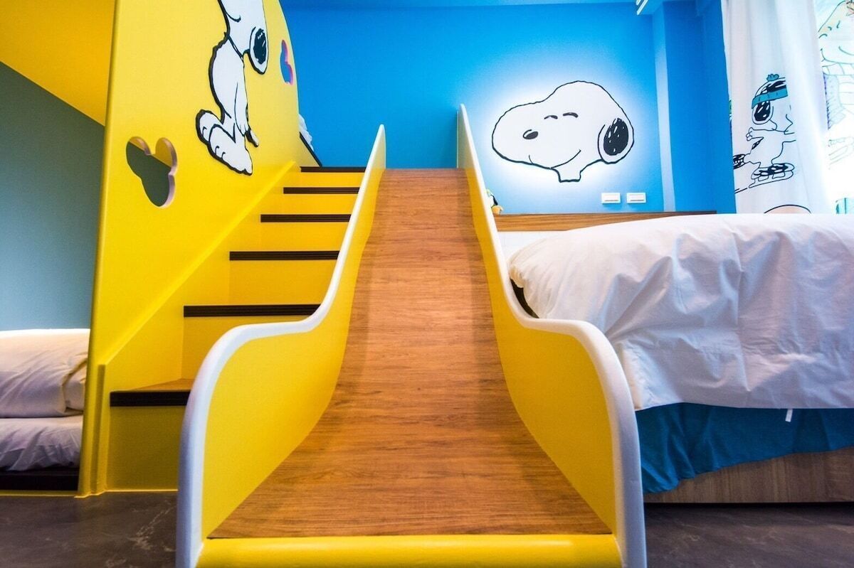 Una habitación infantil con un tobogán, dos camas y decoración de pared temática de Snoopy.