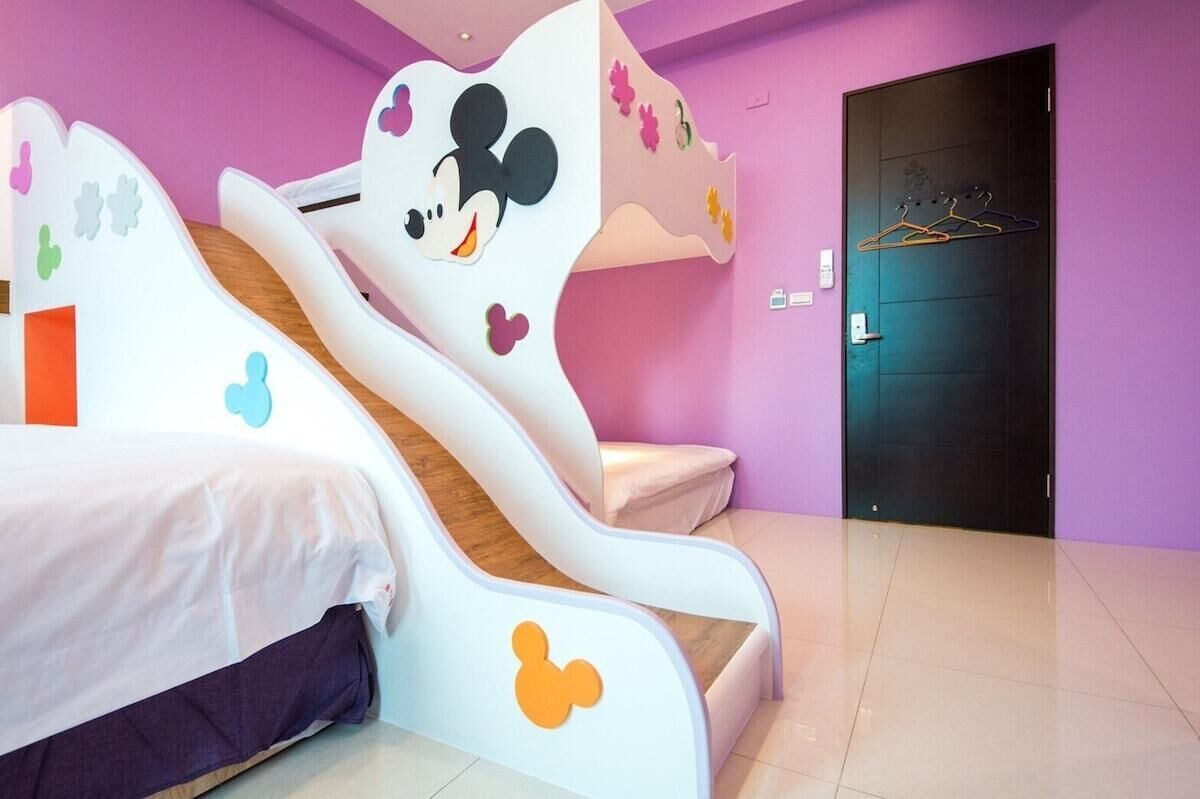 A children's room with a Mickey Mouse-themed bed, a small slide, and a door with a coat rack.