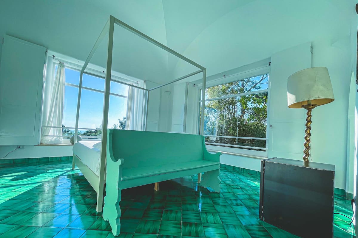 A room with a four-poster bed, large windows, and a green floor.