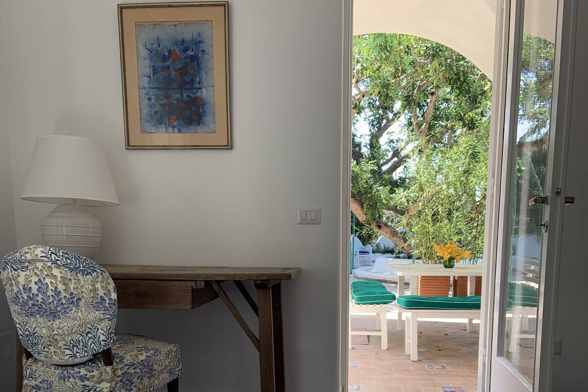 A bedroom with a bed, a desk, a chair, a lamp, and a view of the outdoors.