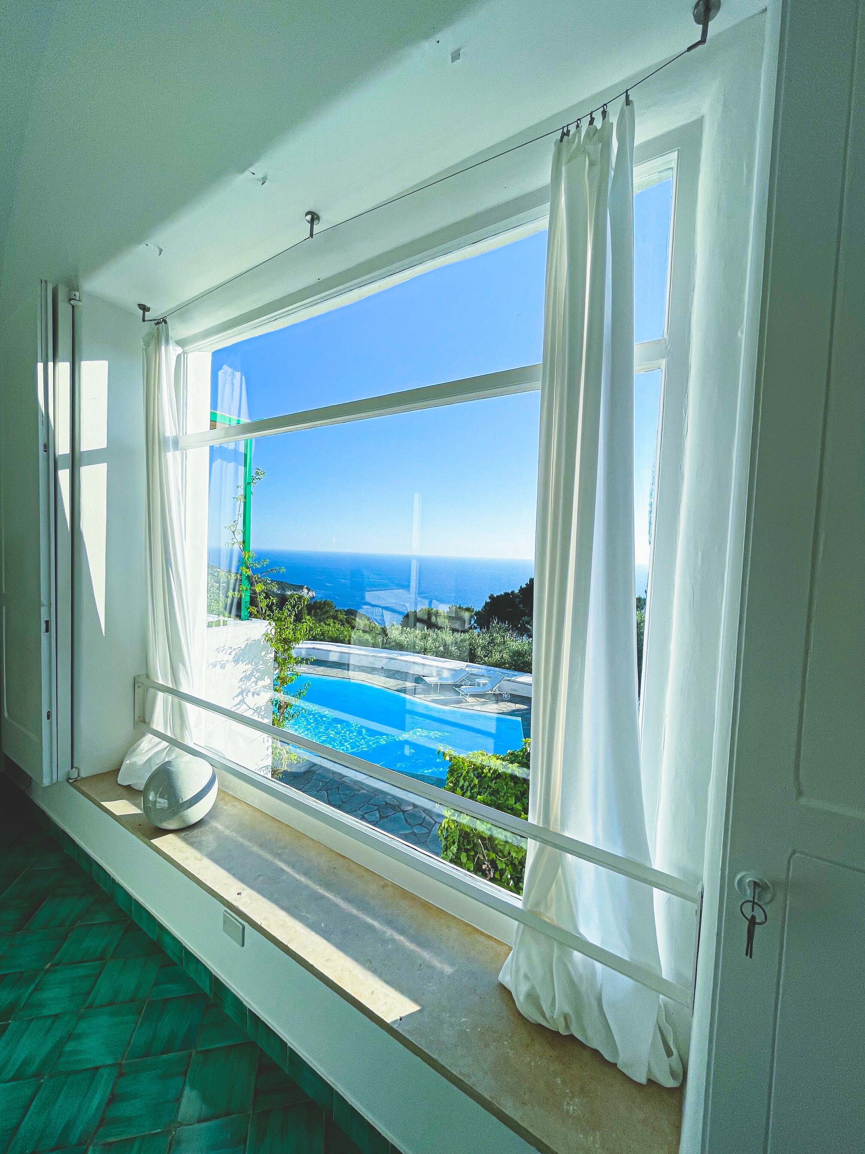 A room with a large window overlooking a pool and a view of the sea.