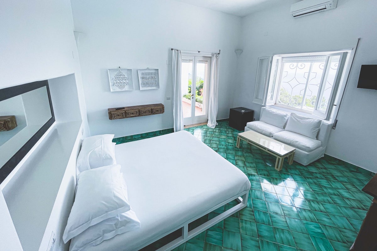 A room with a bed, a sofa, a small table, and a window with curtains.