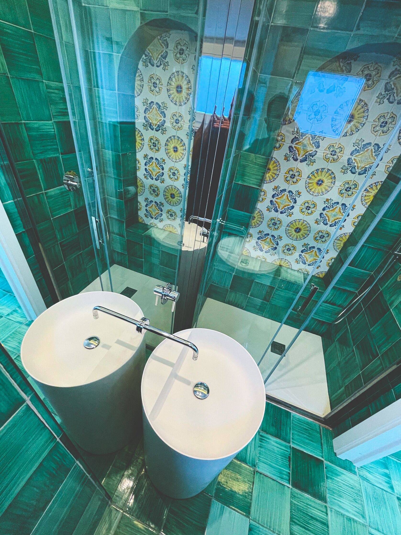 A modern bathroom with two sinks, a glass shower enclosure, and patterned tiles.