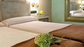 Camera d'albergo con due letti, un comodino con lampada, uno specchio e un bouquet di fiori.