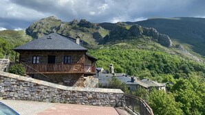 Una casa in pietra con un balcone, immersa nel verde e circondata da montagne.