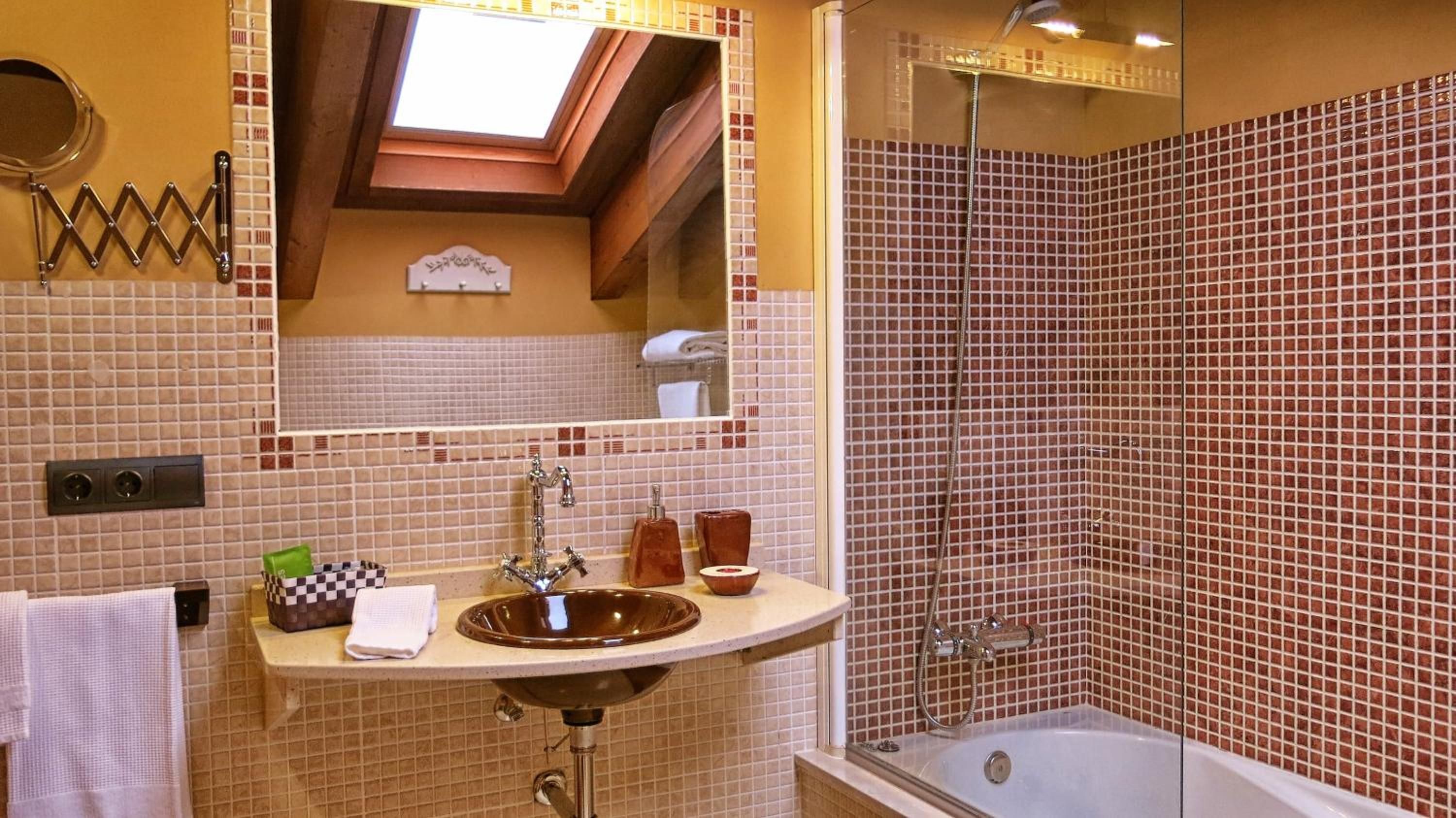 Un baño con un espejo grande, un lavamanos, una ducha y un tragaluz.
