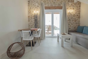 A dining area with a stone wall, white chairs, a wooden table, and a sofa with a cushion.