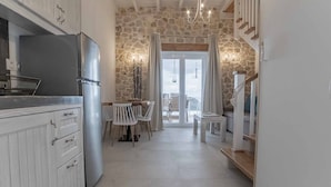 Cuina amb armaris blancs, un refrigerador d'acer inoxidable, taula de dinar amb caires blancs i una paret de pedra.