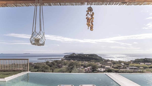 Vista a la piscina amb dues gandules, una làmpada penjant i una vista del mar i el paisatge llunyà.