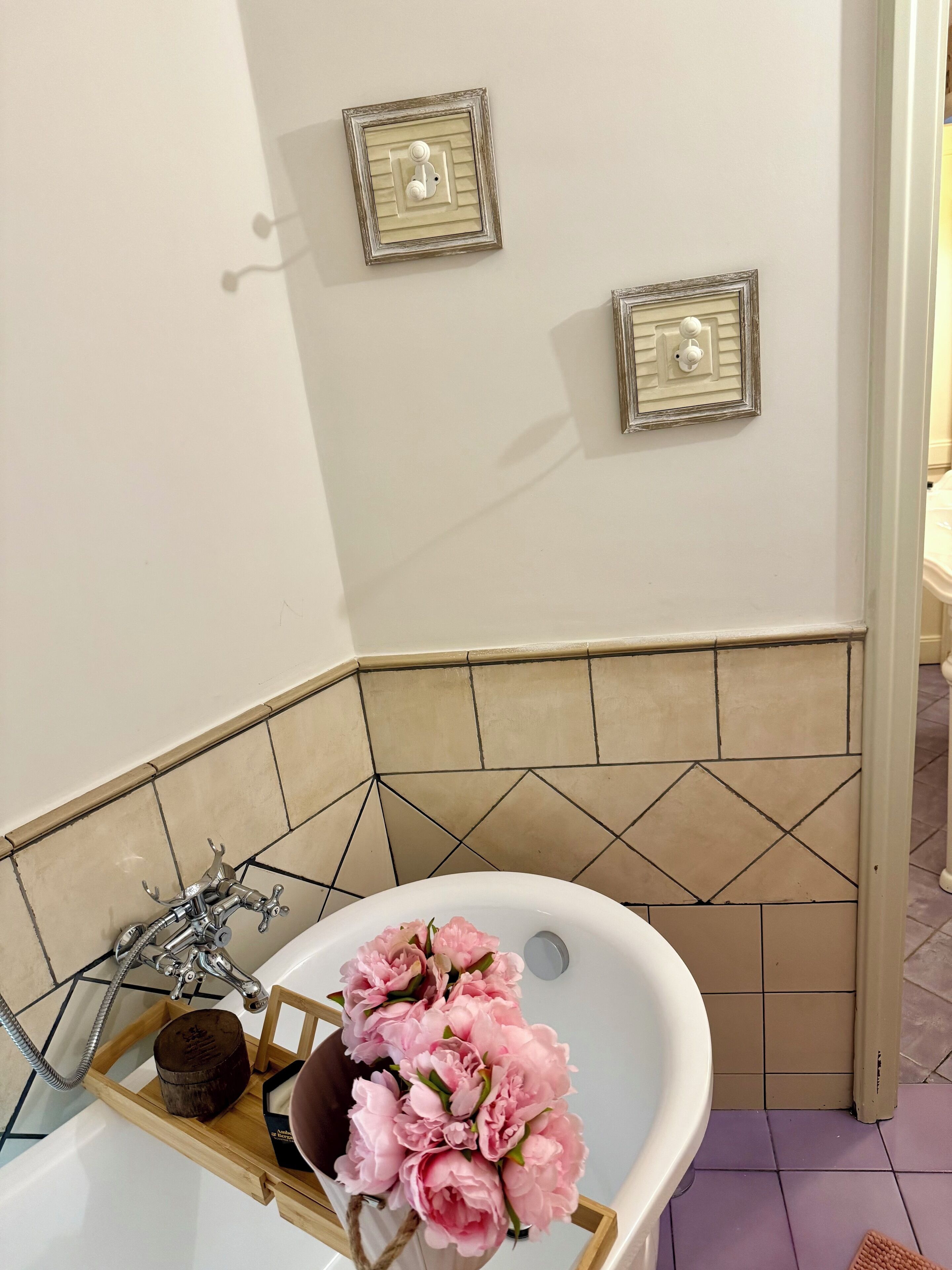 Ein Badezimmer mit einer Badewanne, einem Holztablett mit Blumen und zwei an der Wand befestigten Lichtschaltern.
