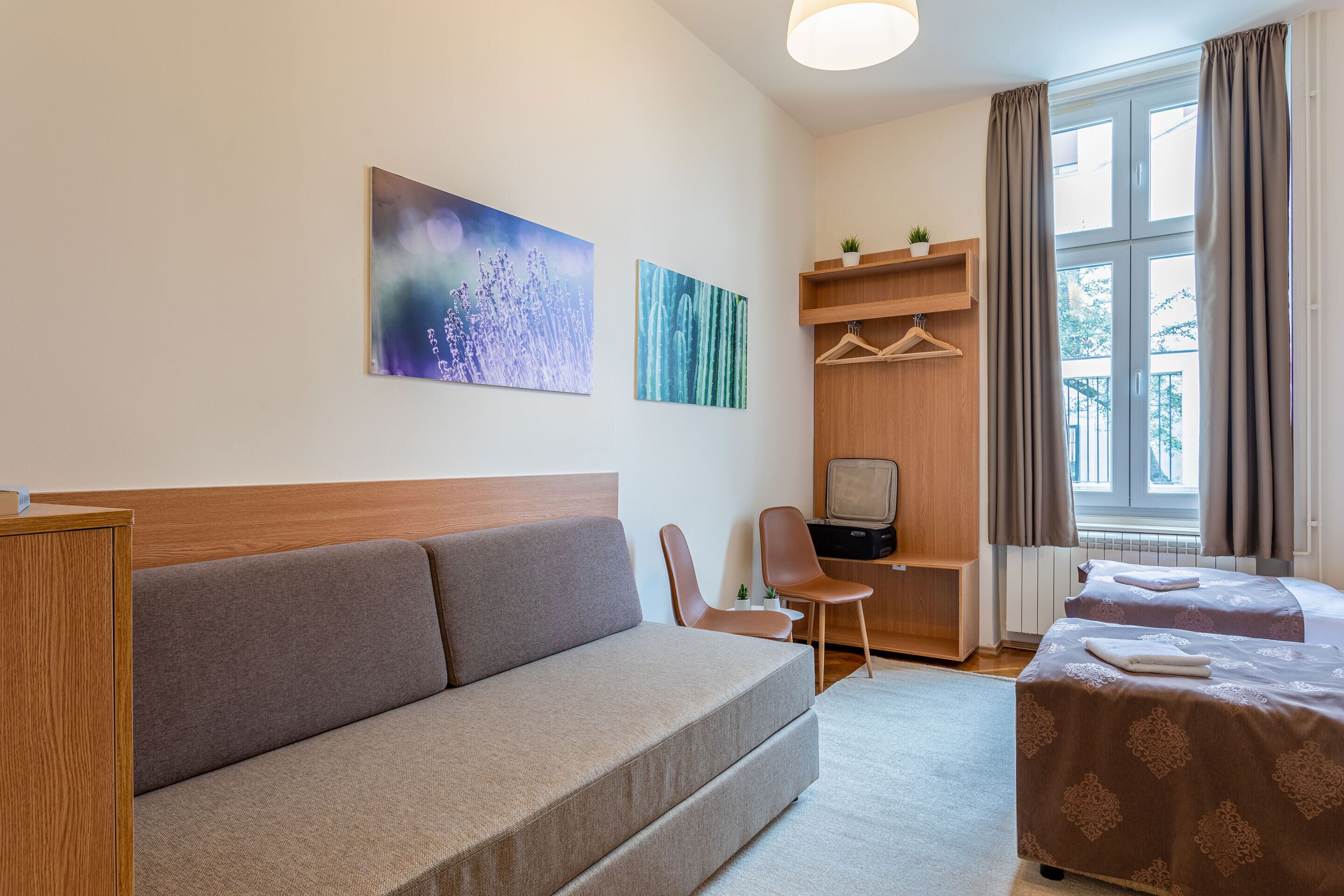 A modern hotel room with a sofa, two beds, a desk, and a TV.