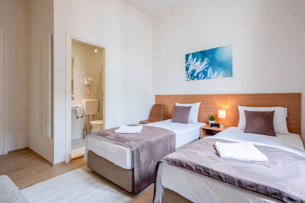 A hotel room with two beds, a bathroom, and a painting on the wall.