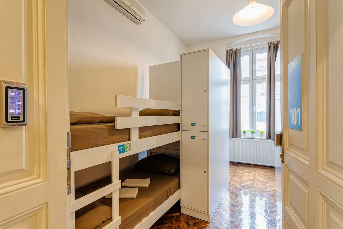 A hotel room with bunk beds, a wardrobe, a digital lock, and a window with curtains.