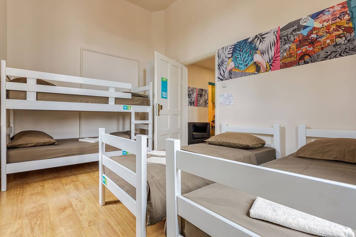 A dormitory room with bunk beds, a door with a number sign, and a wall with a colorful mural.