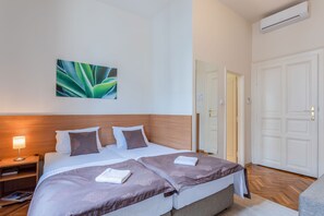 Una cama doble con cabecera, una mesita de noche con lámpara, aire acondicionado de pared y una puerta con espejo.