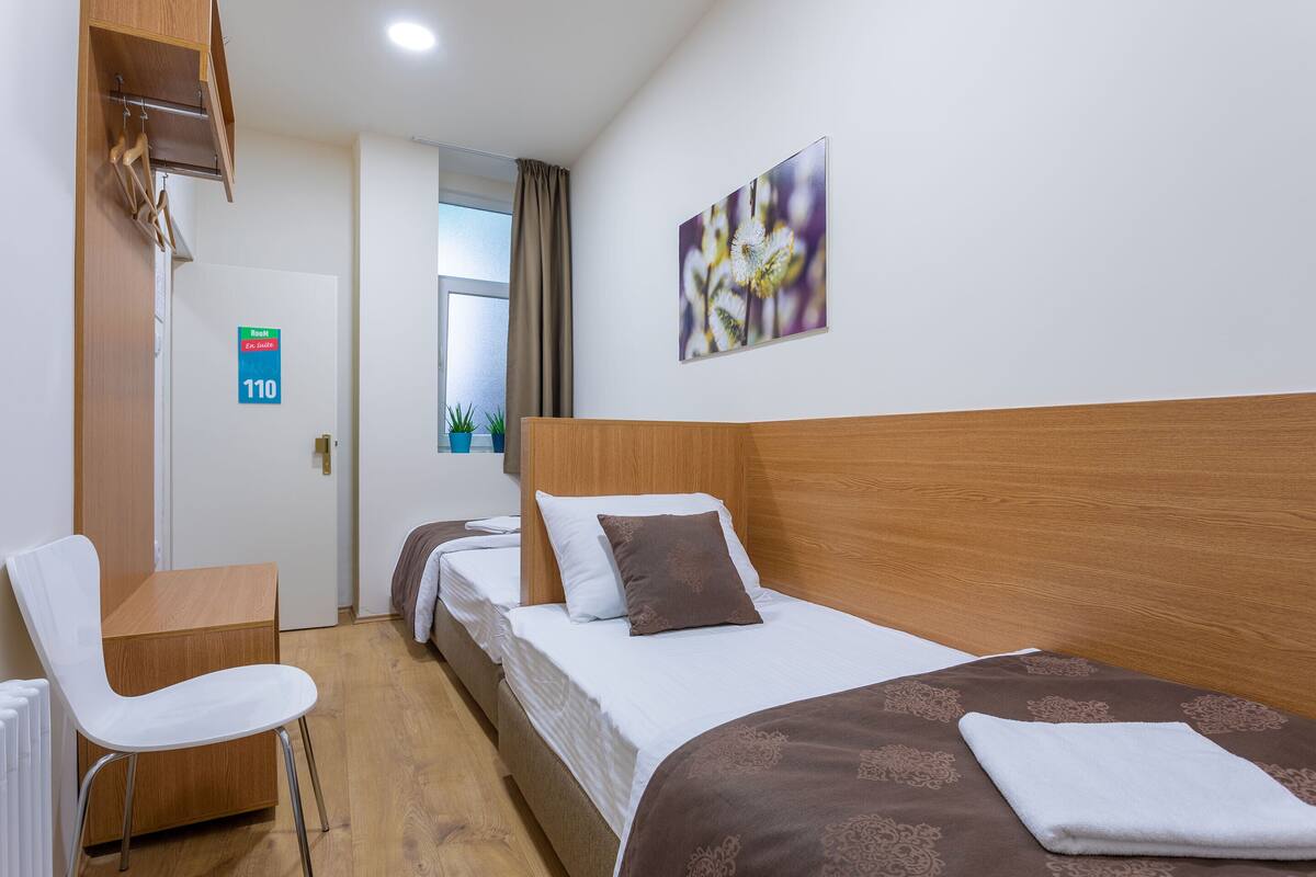 A hotel room with a bed, a desk, and a chair. There is a door with a sign indicating room number 110.