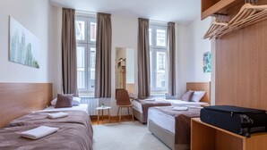 A hotel room with two beds, a small table, a chair, and a wooden wardrobe. - Booking BnB (Belgrade)