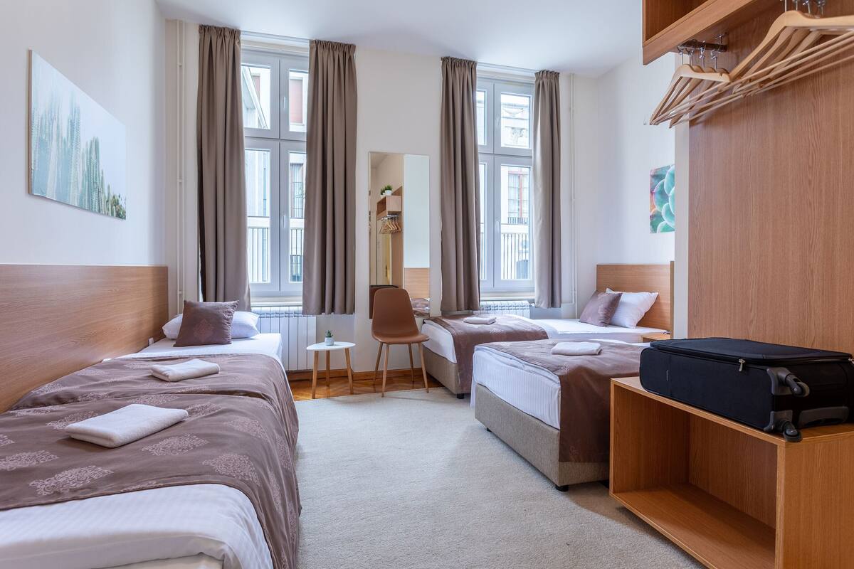 A hotel room with two beds, a small table, a chair, and a wooden wardrobe.