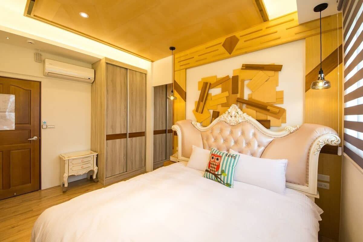 A bedroom with a large bed, a wooden headboard, a small bedside table, and a wall-mounted air conditioner.