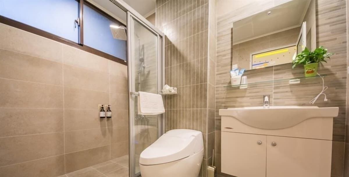 A modern bathroom with a glass shower enclosure, a white toilet, a sink with a mirror, and a potted plant.