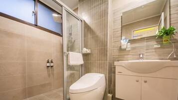 A modern bathroom with a glass shower enclosure, a white toilet, a sink with a mirror, and a potted plant.