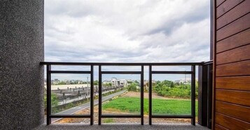 A balcony with a view of a road and greenery, a building in the distance, and a cloudy sky.