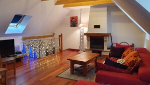 A cozy loft-style living room with a wooden ceiling, a fireplace, a red sofa, and a TV on a wooden stand. - House / Villa - VIGNEC (Vignec)