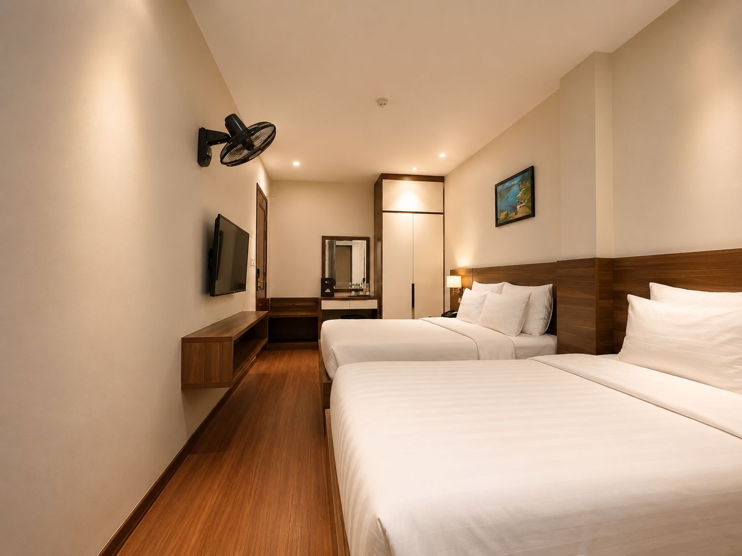 A hotel room with two beds, a TV, a desk, a mirror, and a painting on the wall.