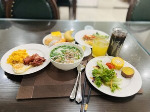 A table with various dishes including a bowl of soup, plates of food, and a glass of juice. - Paragon Noi Bai Hotel and Pool (Hanoi)
