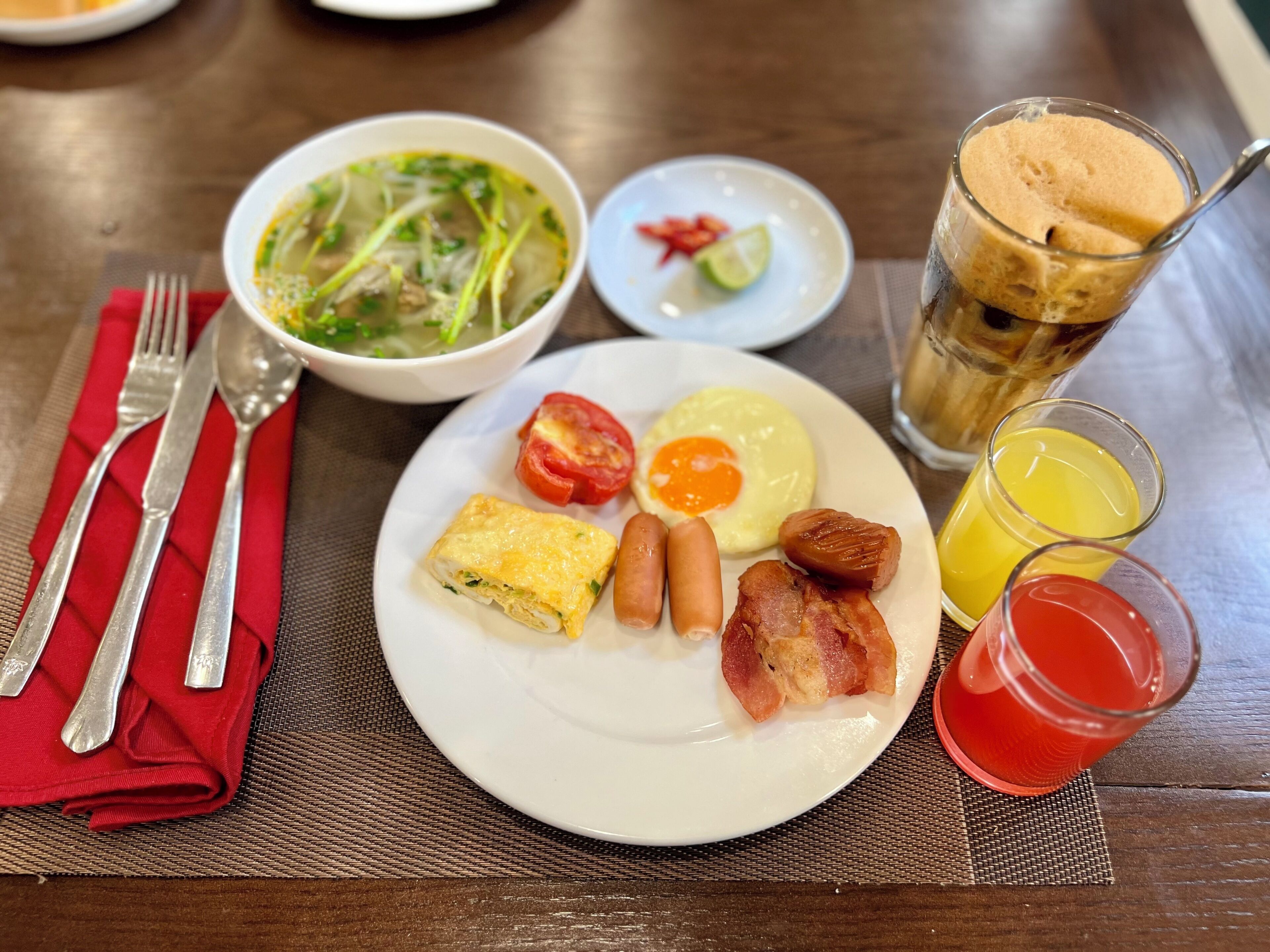 A breakfast plate with eggs, sausages, bacon, and a bowl of soup.