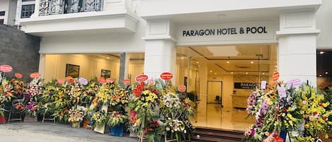 Exterior del Hotel Paragon y su piscina, con varios arreglos florales al frente.