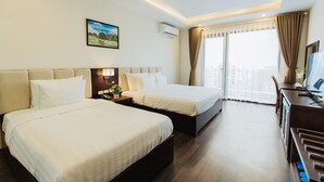 Una habitación de hotel con dos camas, un escritorio y un ventanal grande con cortinas.