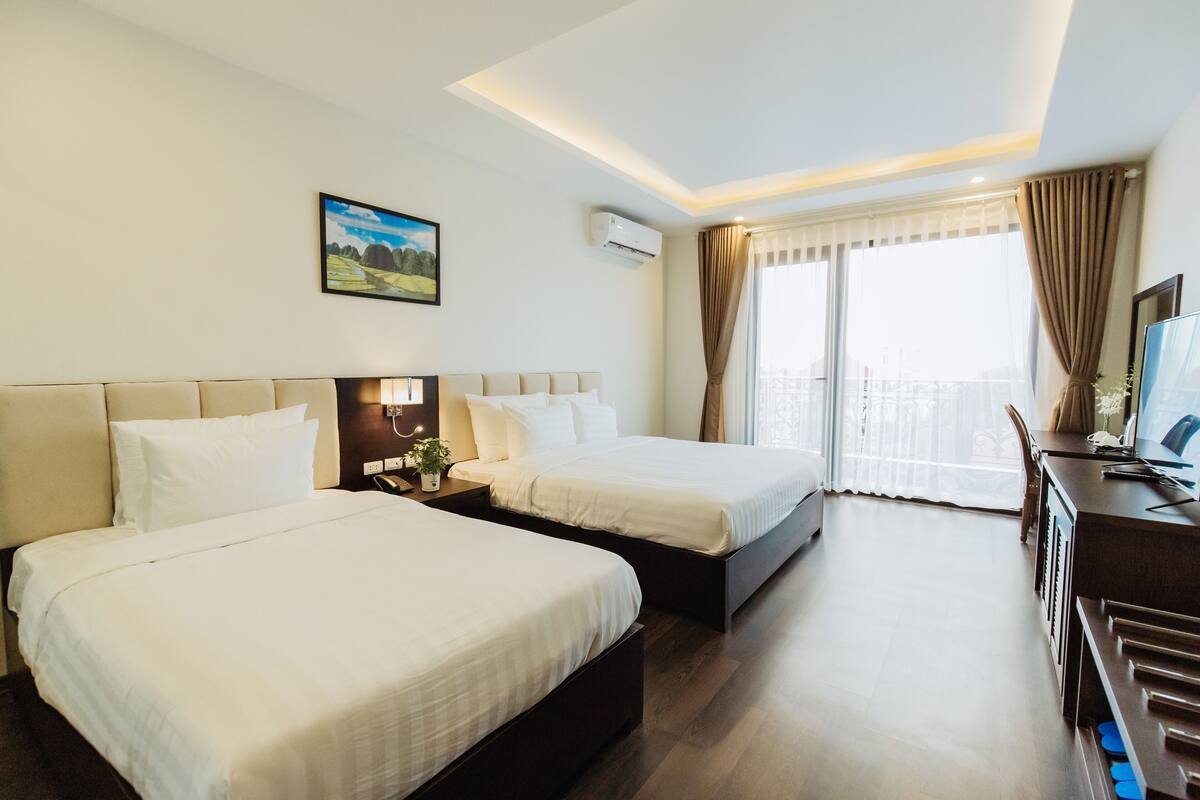 Una habitación de hotel con dos camas, un escritorio y un ventanal grande con cortinas.