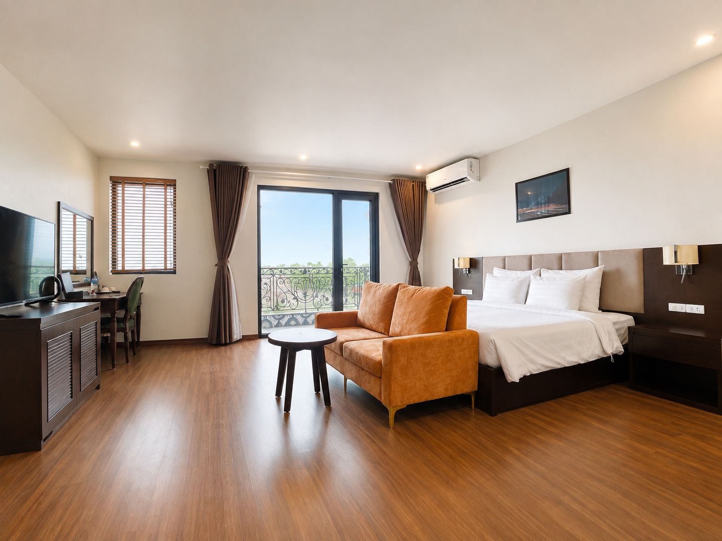 Habitación de hotel con cama, sofá, escritorio con televisor y balcón con cortinas.