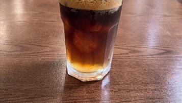 Un vaso de café helado sobre una mesa de madera en un restaurante, con sillas y una ventana al fondo.