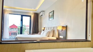 Una camera d'albergo con un letto, una finestra con tende, un condizionatore d'aria a muro e un quadro.