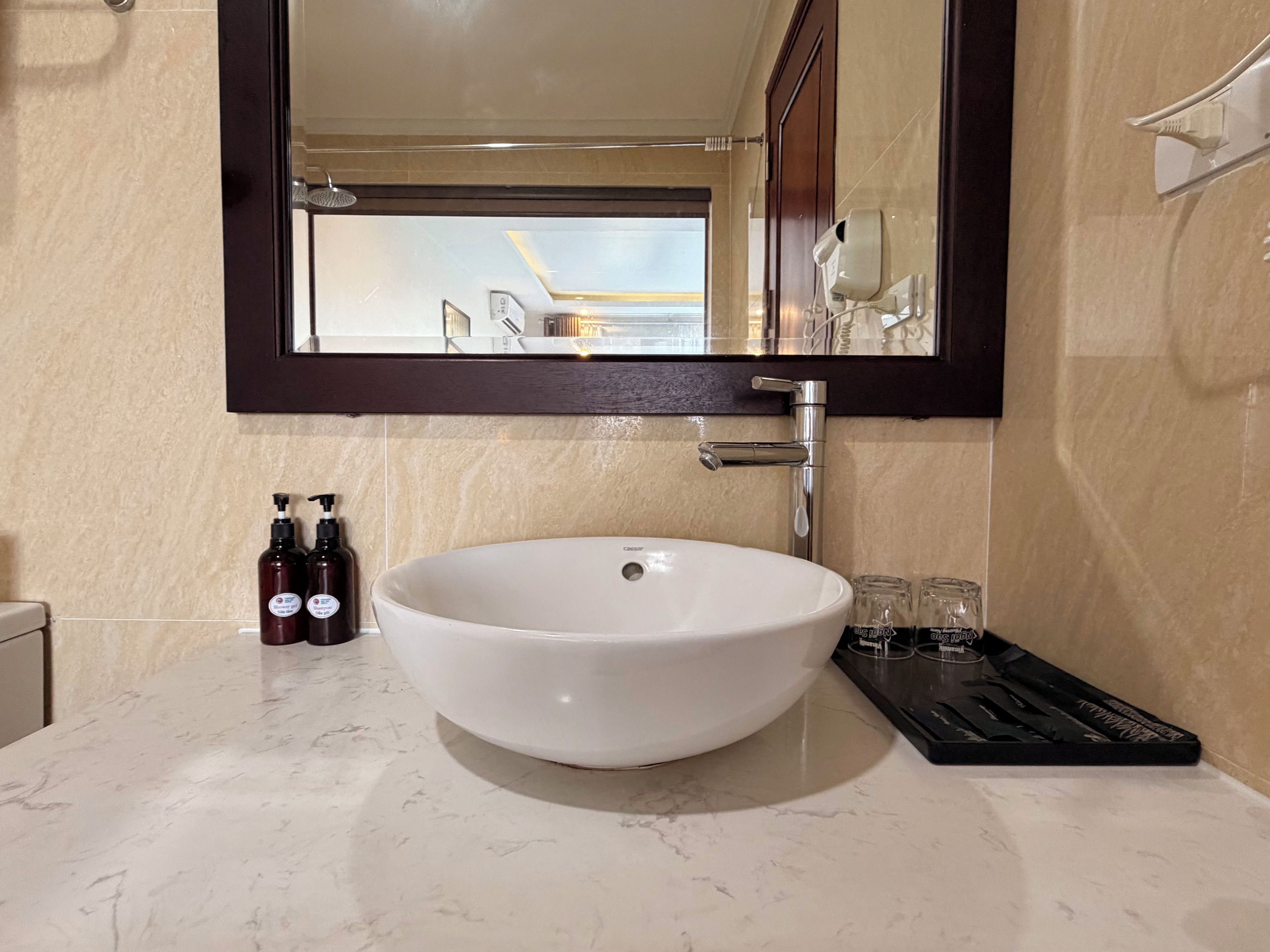 A bathroom with a large white sink, a mirror, and a towel rack. There are two bottles of shampoo and two glasses on the counter.