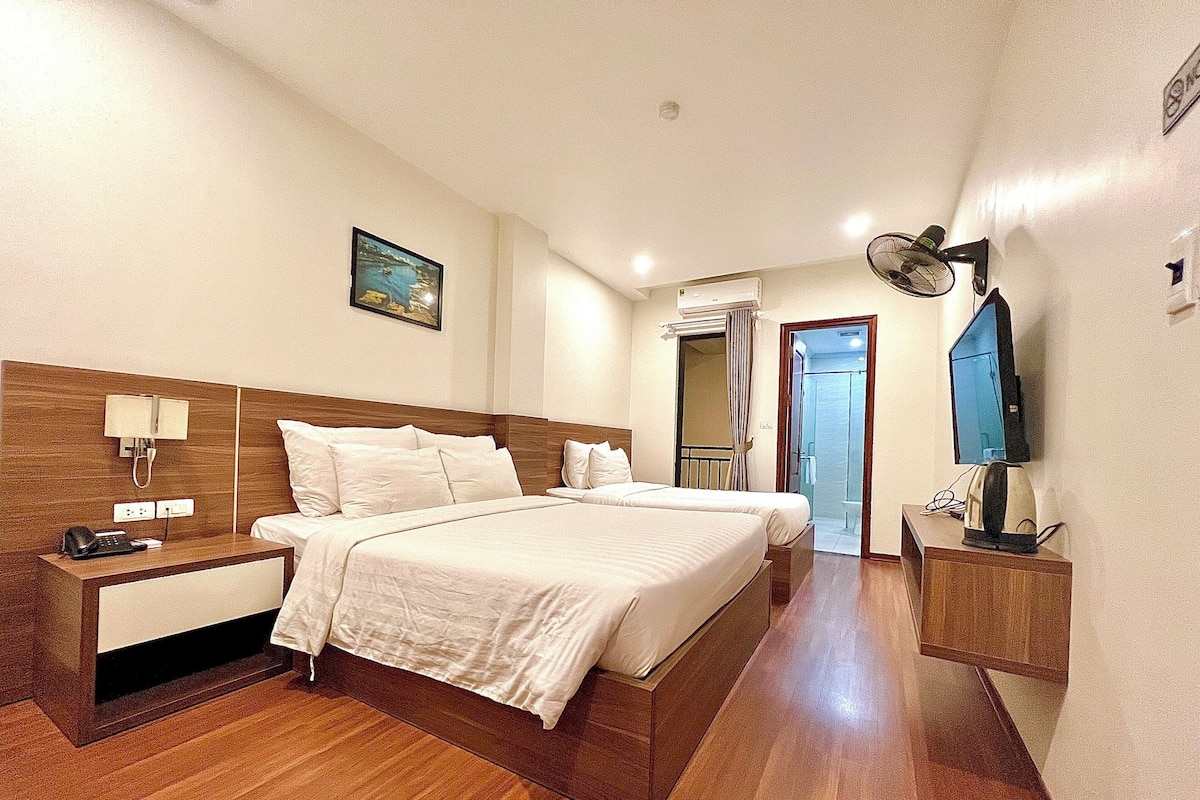 Habitación de hotel con una cama grande, mesitas de noche, un escritorio con computadora, televisor y zona de ducha.