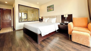 A hotel room with a large bed, a nightstand, a chair, a mirror, and a painting on the wall. - Paragon Noi Bai Hotel and Pool (Hanoi)