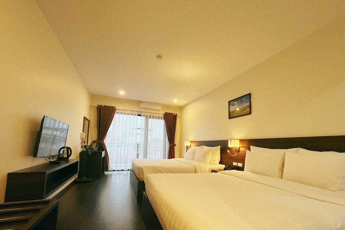Habitación de hotel con dos camas, un televisor, un escritorio con lámpara y una ventana con cortinas.