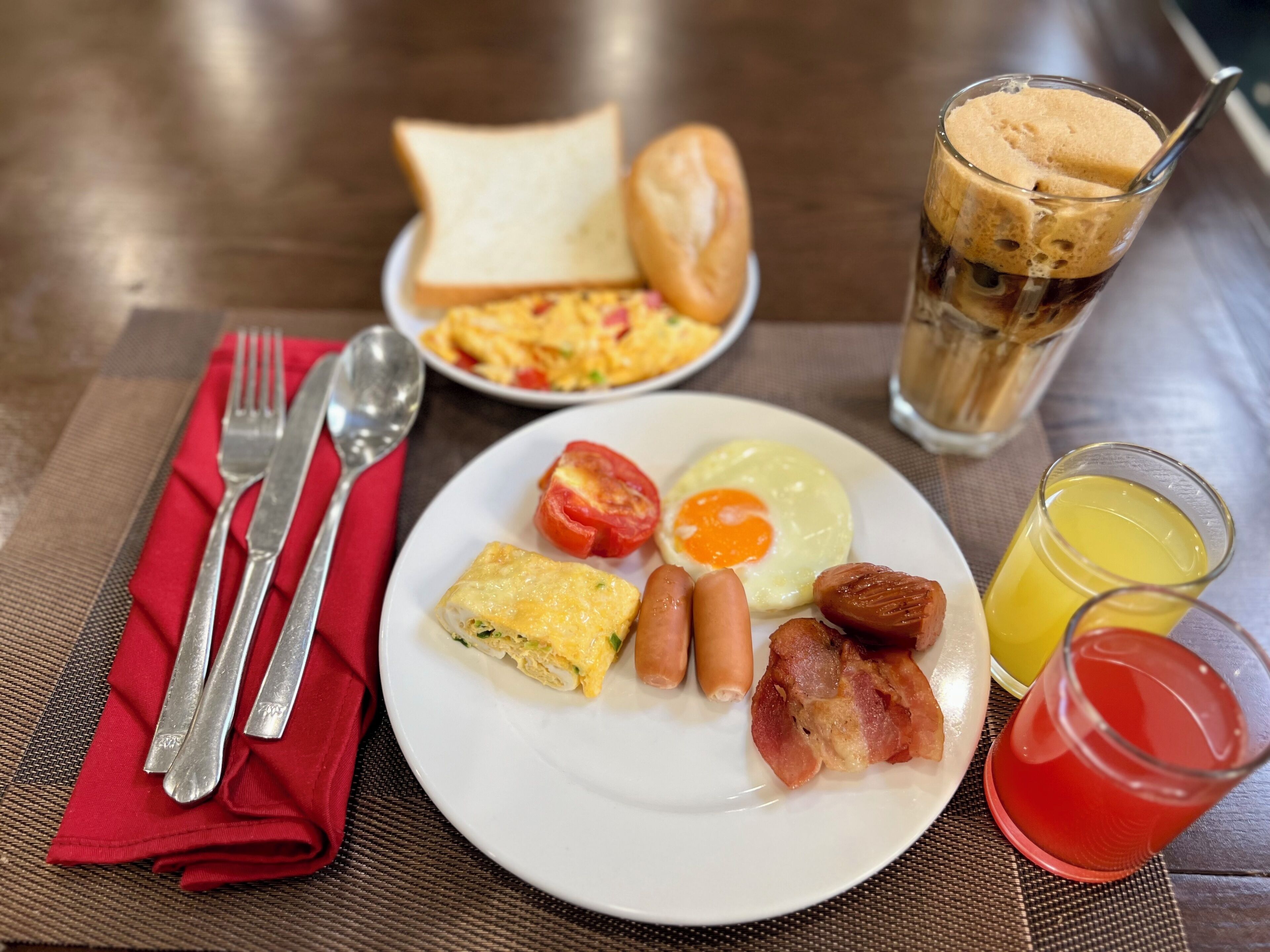 A breakfast plate with eggs, bacon, sausages, and a glass of orange juice.