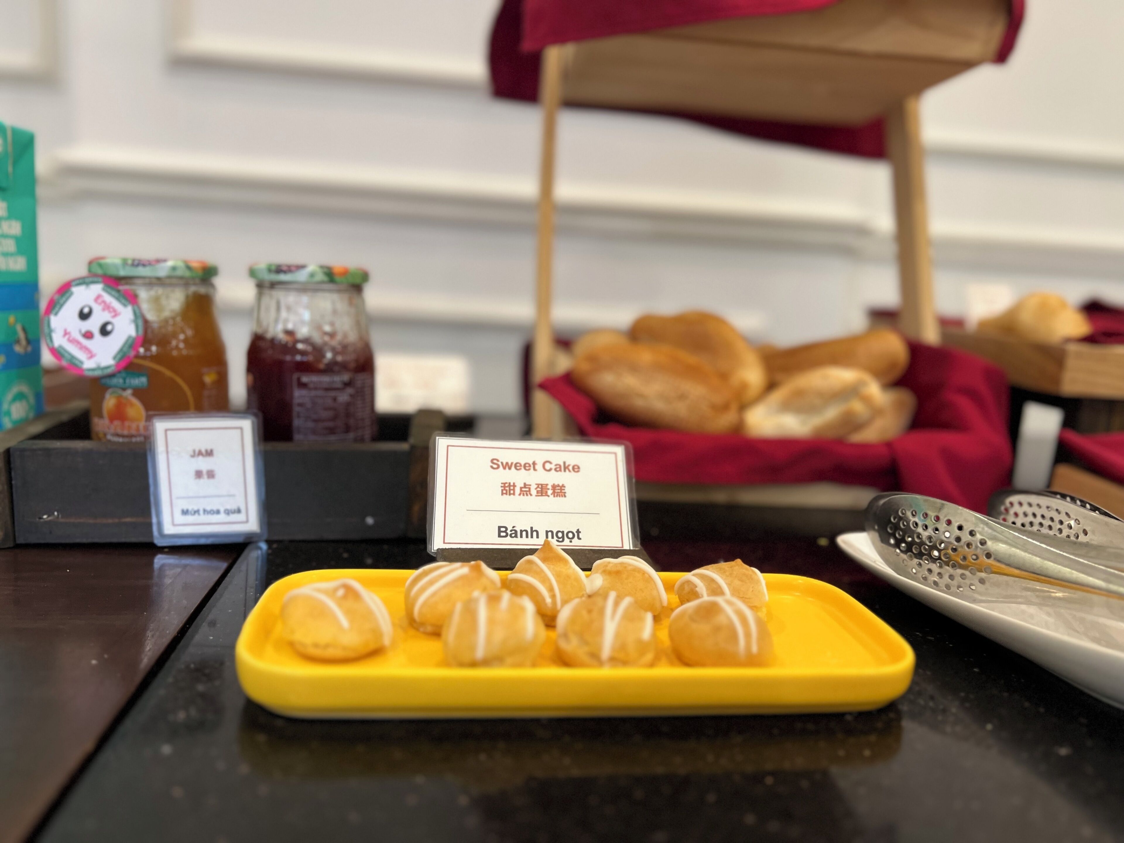 A display of food items including a yellow plate with sweet cakes, a jar of jam, and a sign with text in a foreign language.