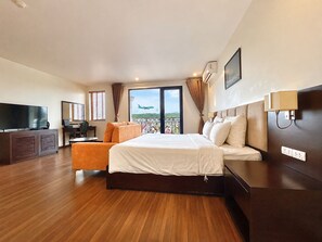A hotel room with a large bed, a television, a desk with a chair, and a balcony with a view of the sky and greenery. - Paragon Noi Bai Hotel and Pool (Hanoi)