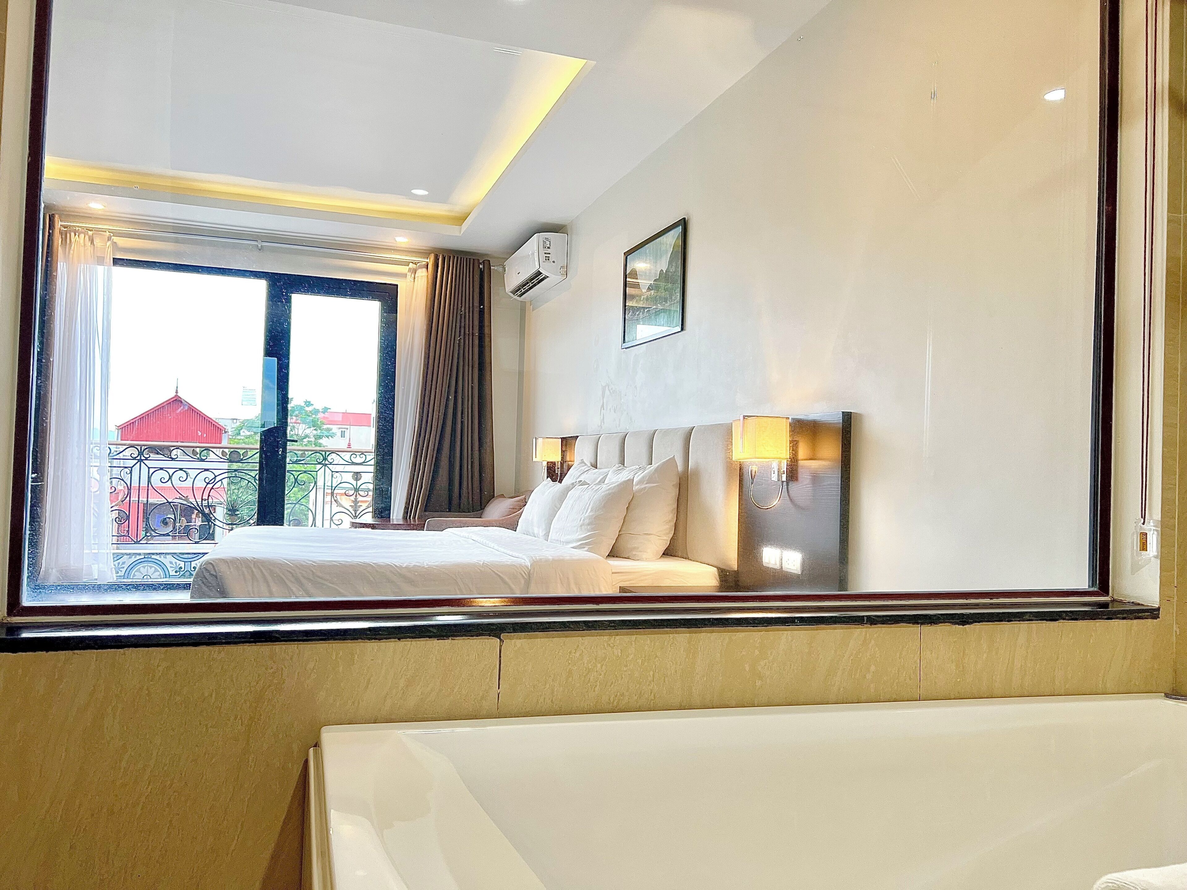 A hotel room with a bed, a window, a wall-mounted air conditioner, and a picture.