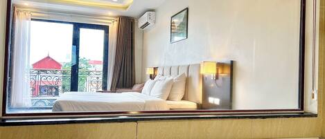 A hotel room with a bed, a window, a wall-mounted air conditioner, and a picture.