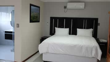 Una habitación de hotel con una cama grande, una mesita de noche, un aire acondicionado de pared y un cuadro enmarcado en la pared.