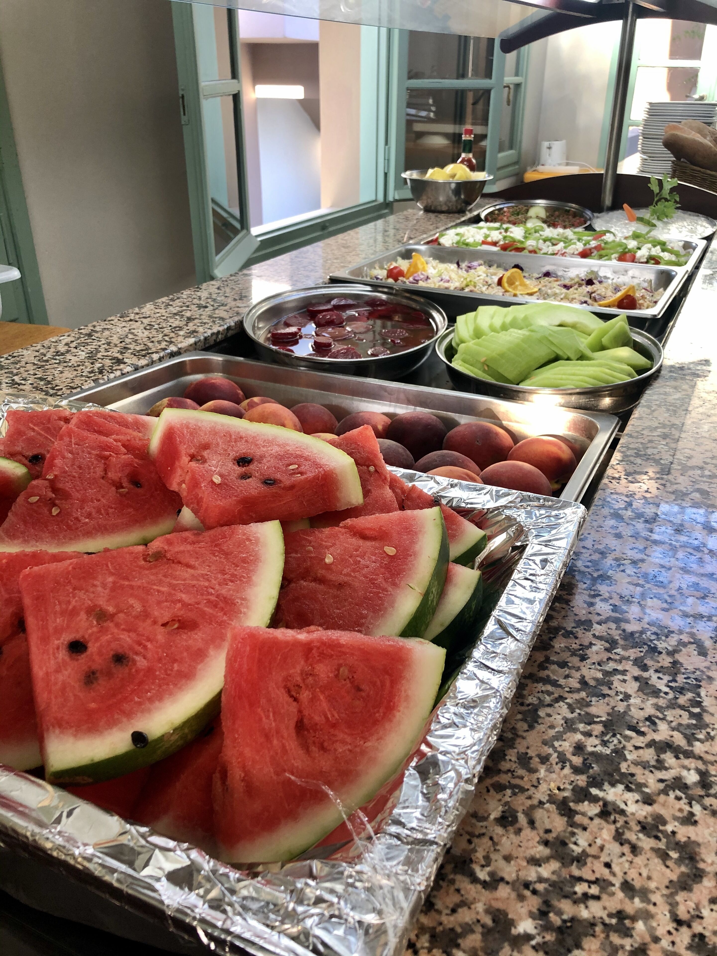 Buffet com diversos alimentos, incluindo melancia, uvas e saladas.