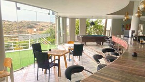 Un espace bar moderne doté d’une table de billard, de sièges et offrant une vue sur l’extérieur.